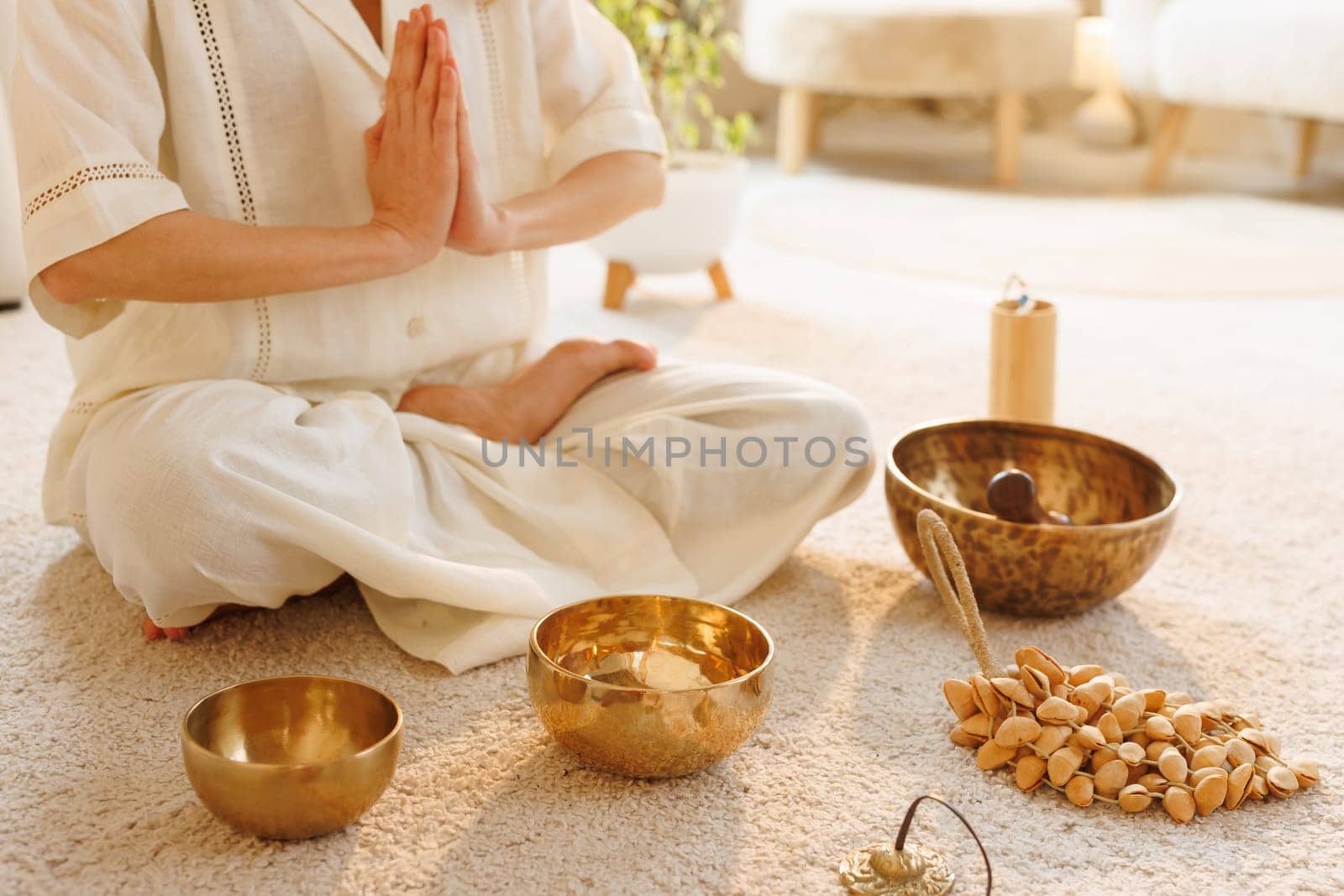 Woman meditating in lotus pose with prayer hands, surrounded by sound bowls and natural wellness tools.