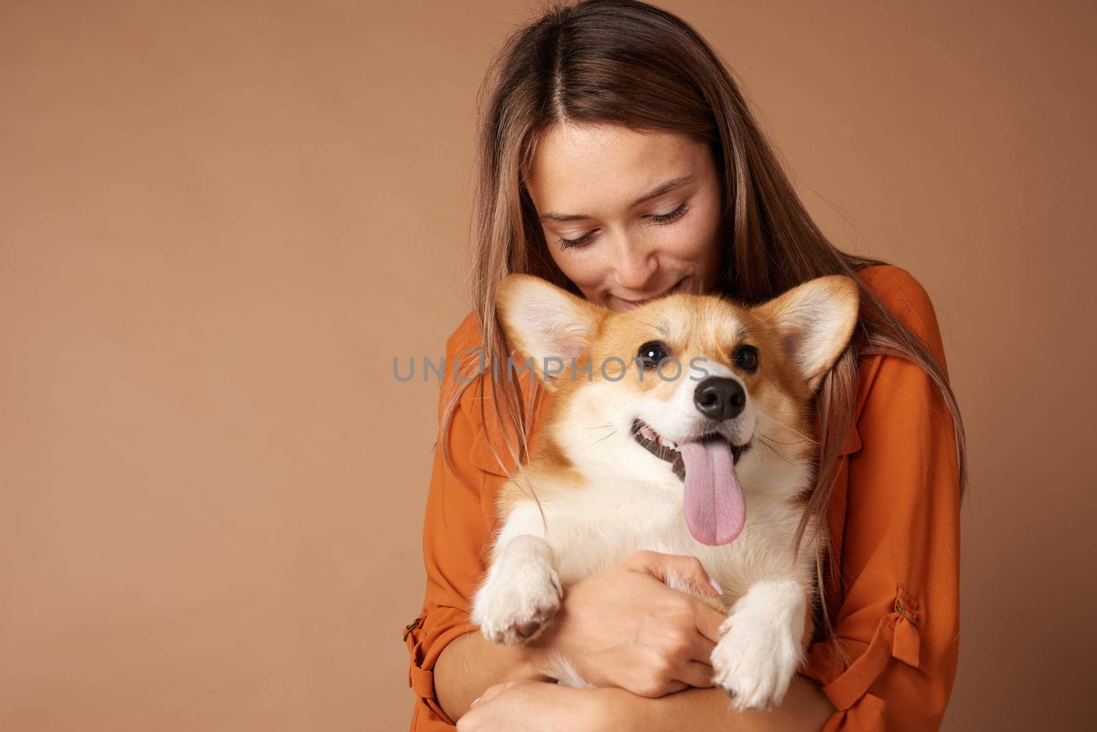 Smiling young woman hugging happy Corgi dog with tongue out, expressing love, affection, and pure joy.
