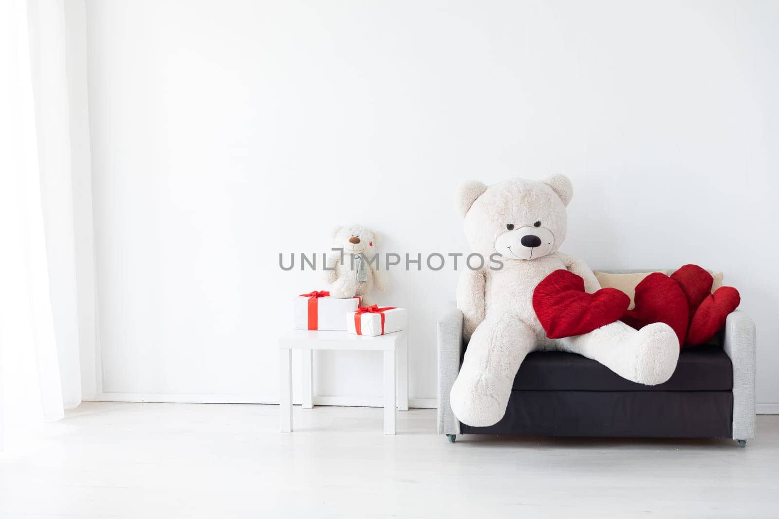 Gray office sofa with flowers and gifts in the interior of a white room with a window