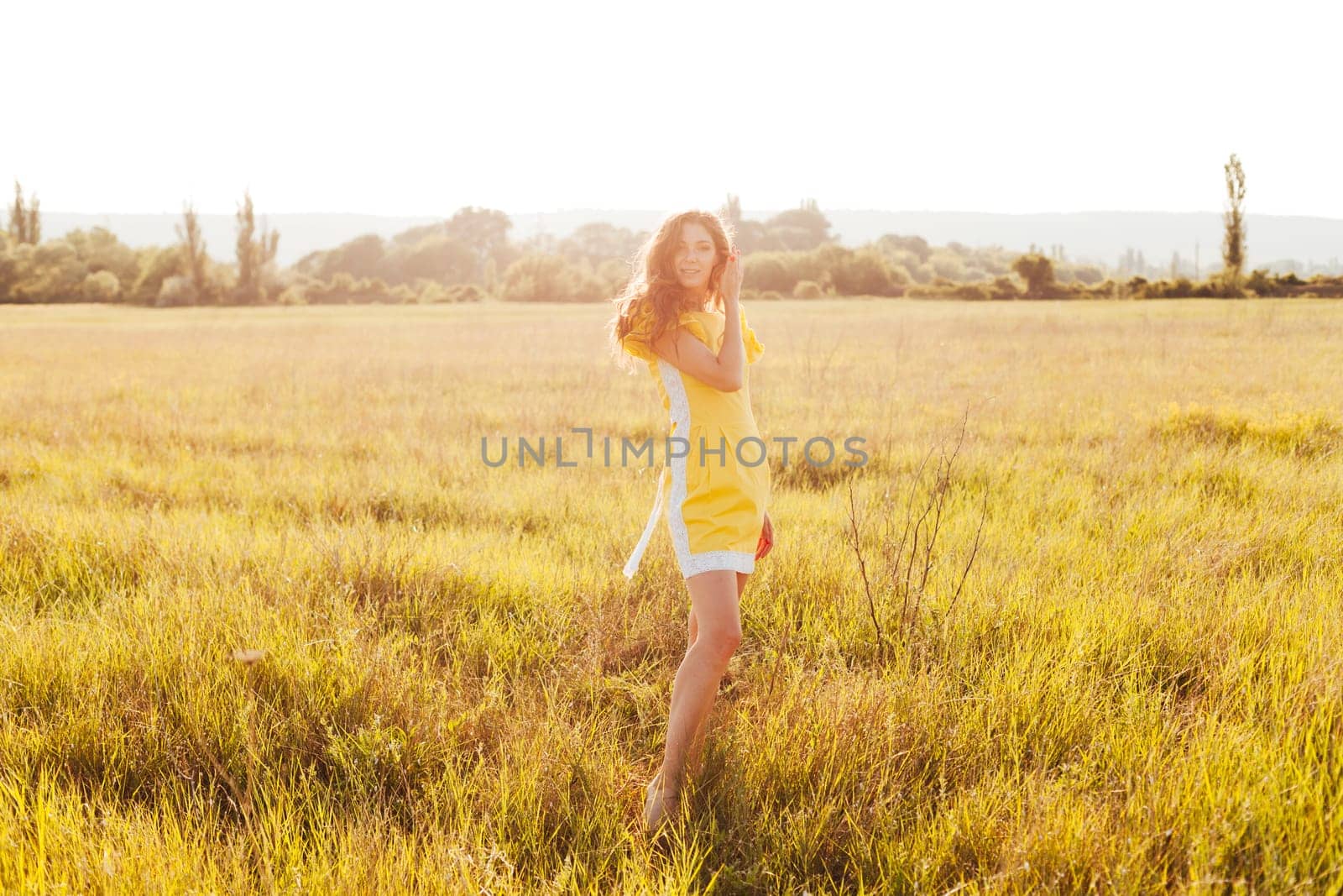 woman in yellow summer dress walking in wheat field at sunset