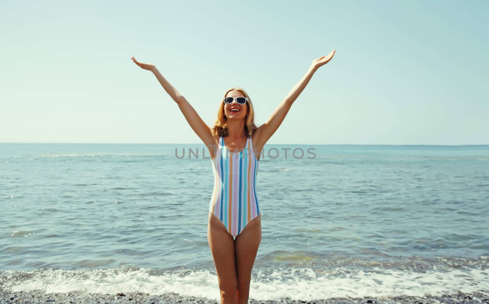 Summer vacation, beautiful happy slim cheerful woman in swimsuit having fun on the beach on sunny day on sea coast with waves background