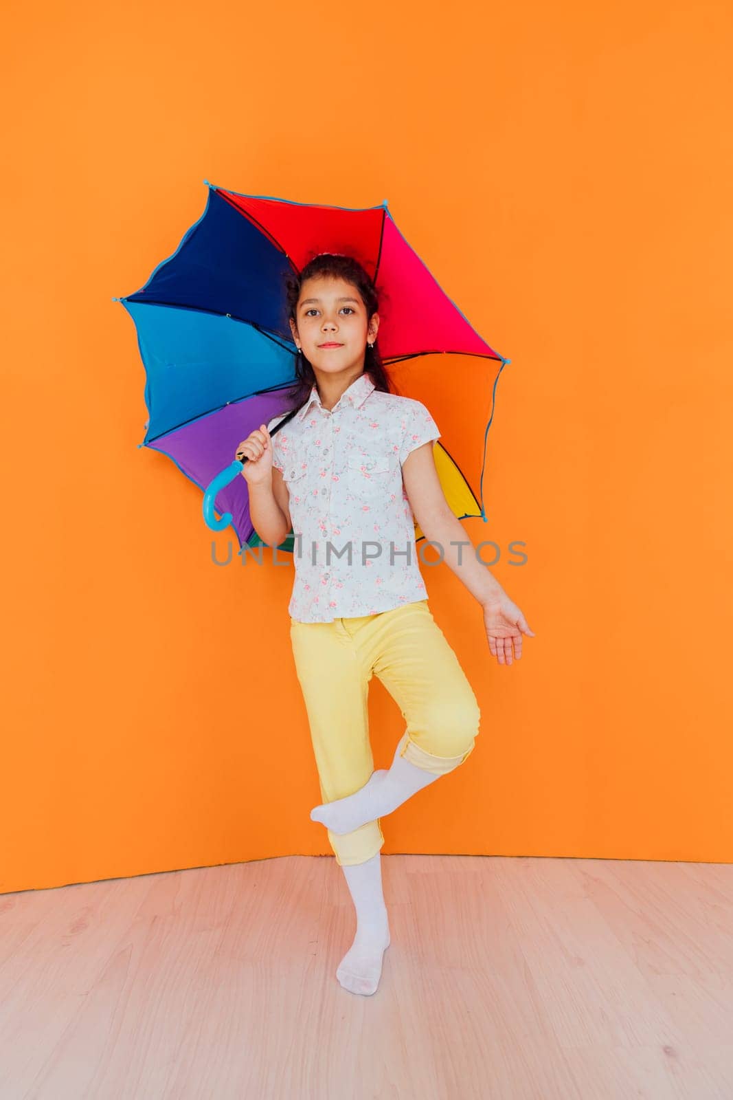 Little girl with colorful rain umbrella on orange background