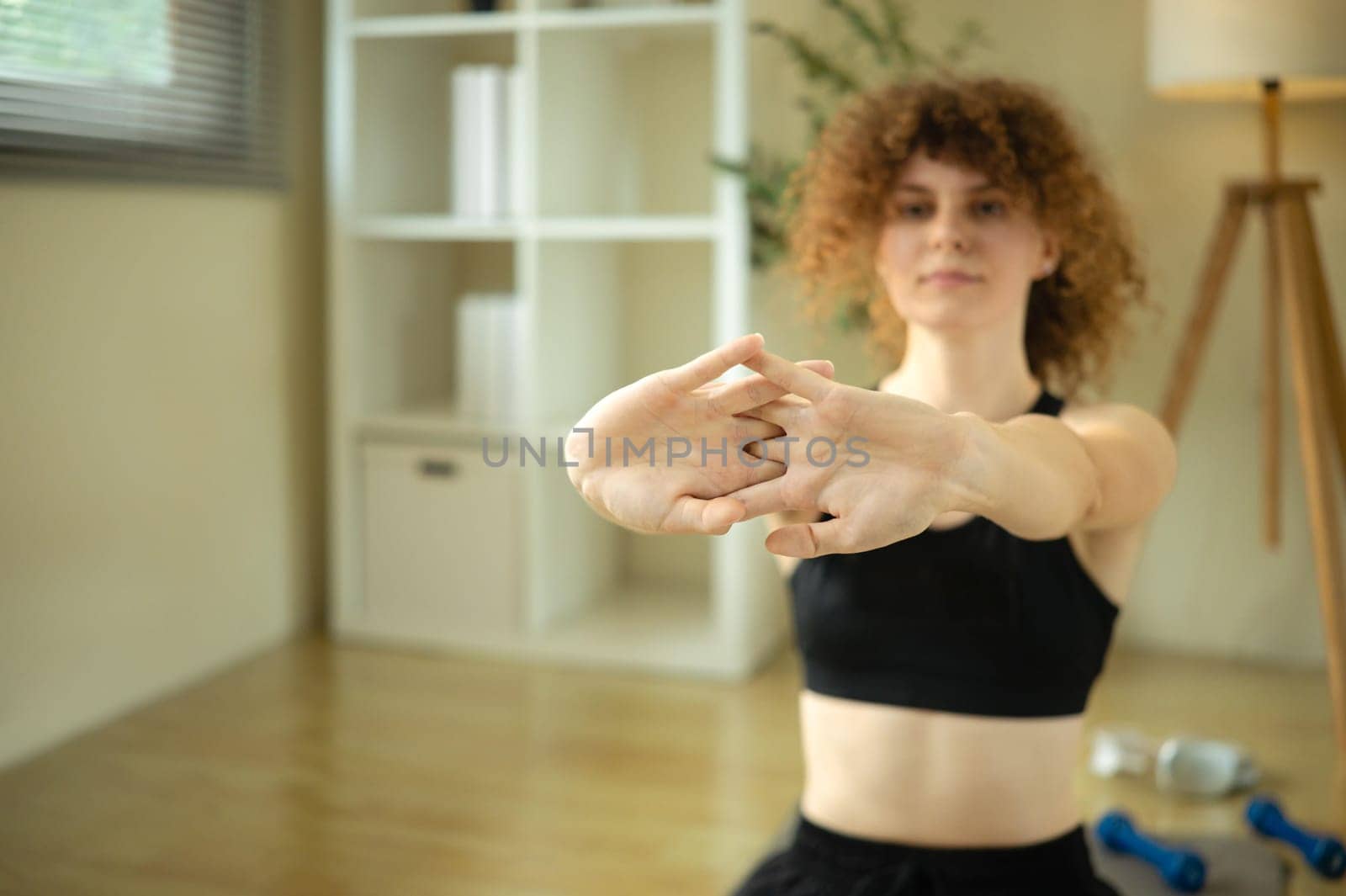 Fit young woman in sportswear doing arm stretches in a cozy home.
