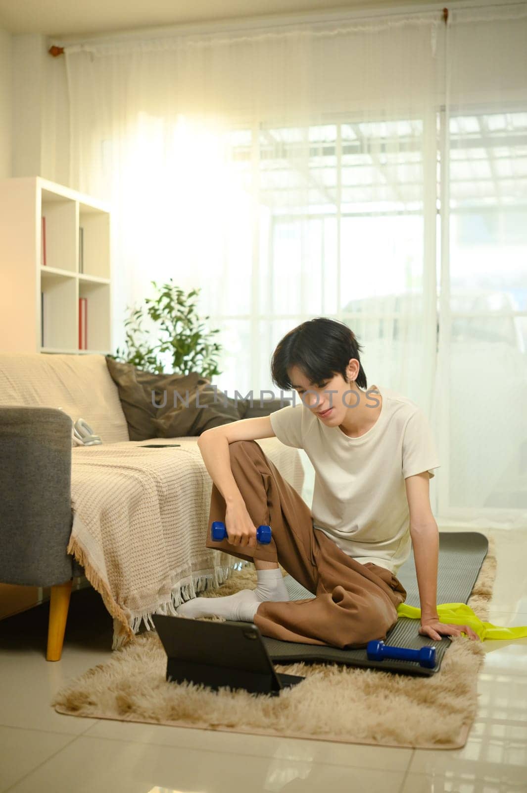 Young man following an online workout while lifting dumbbells at home.