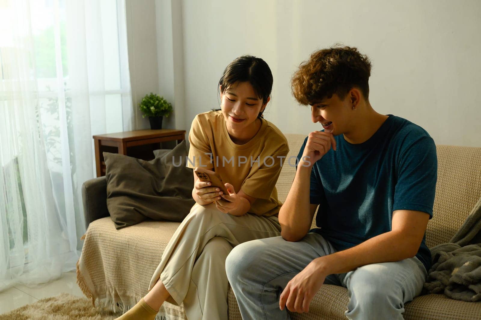 Relaxed couple sitting on couch together and looking at a mobile phone in a living room.