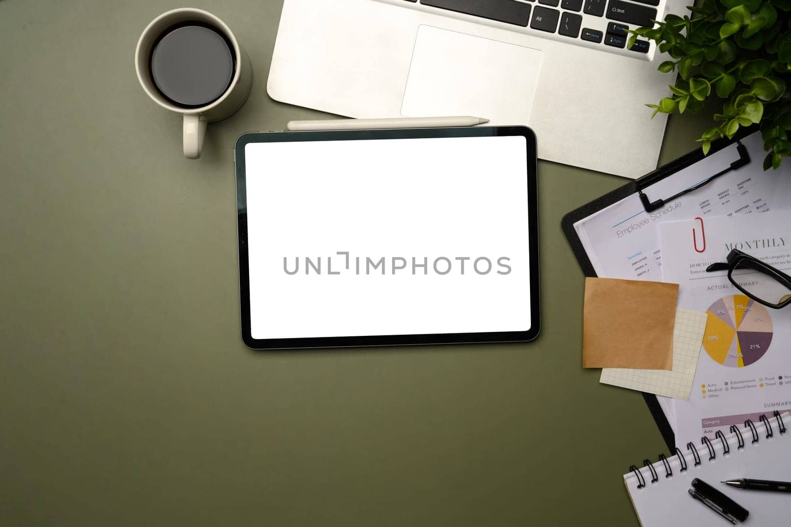 Digital tablet with blank screen surrounded by laptop, financial charts, and office supplies.