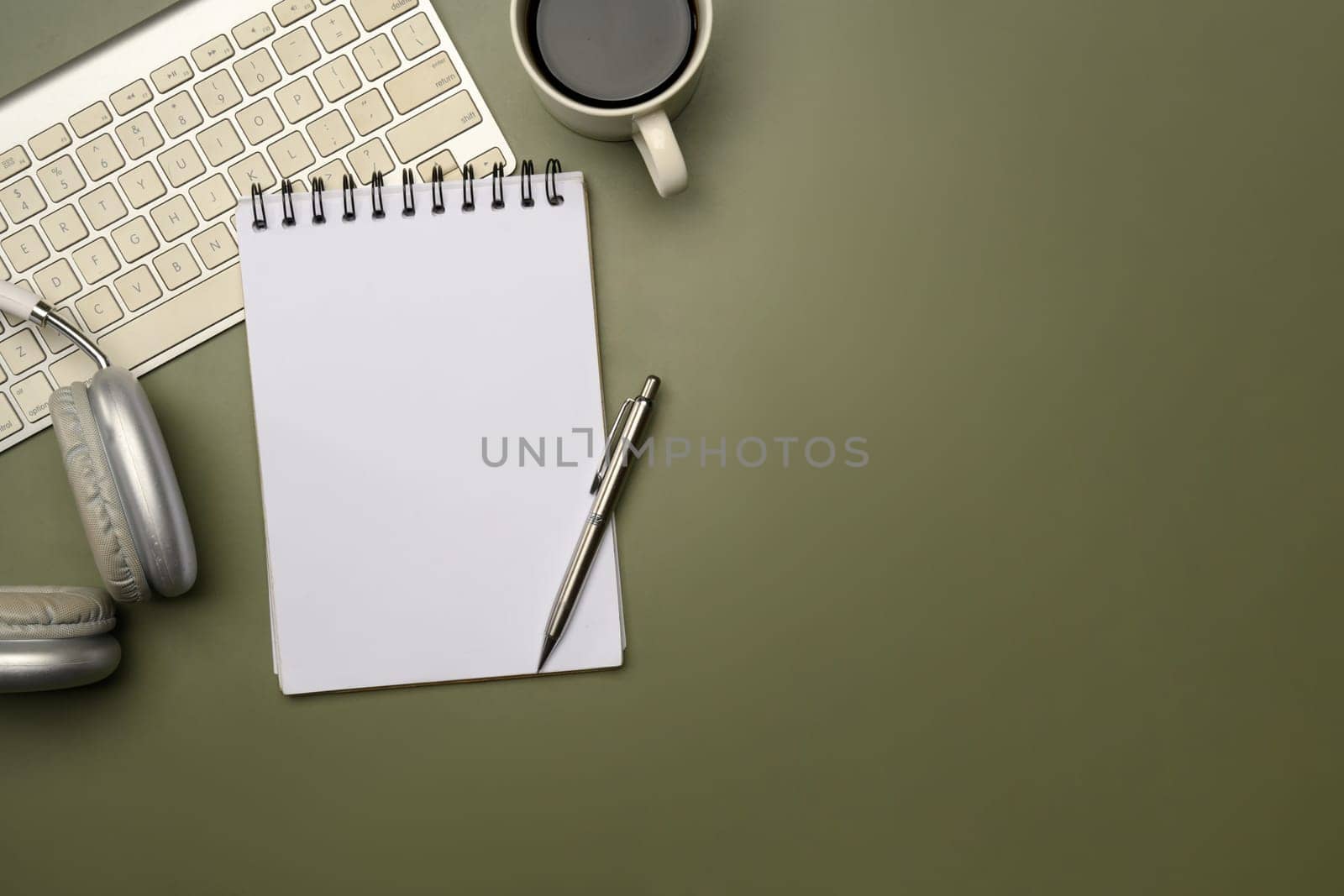 Modern workspace with headphones, coffee mug, and spiral notebook on green surface.