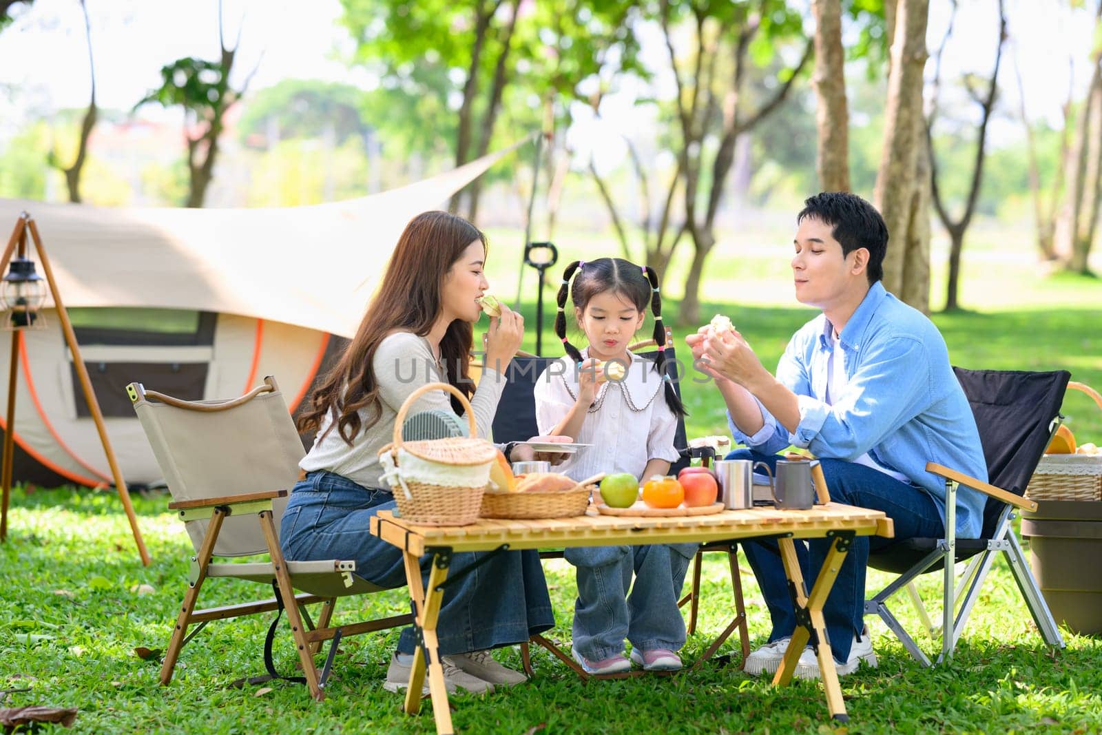 Cheerful family camping outdoors, sharing snacks and spending quality time near tent in the park..
