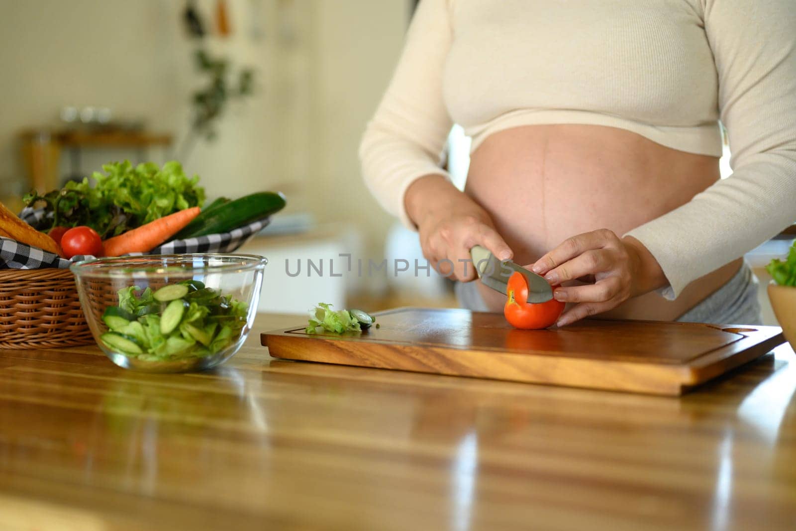 Pregnant woman preparing a fresh vegetable salad in the kitchen.