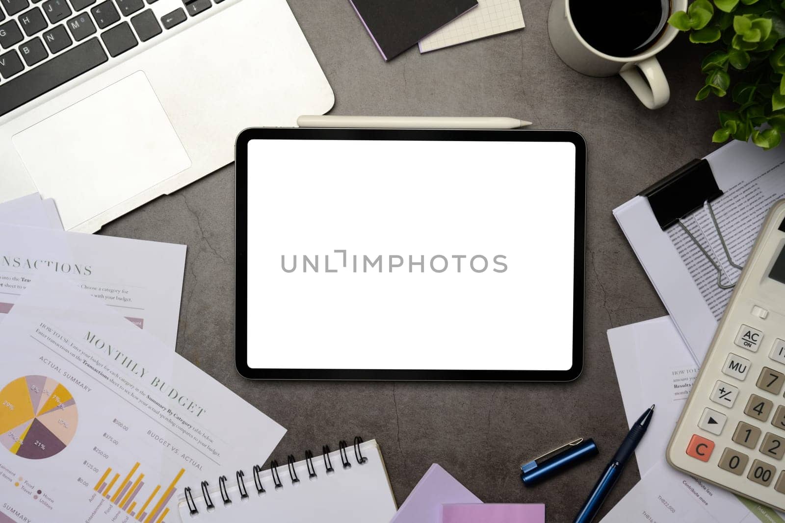 Digital tablet with blank screen surrounded by business documents, laptop, and calculator on office desk.