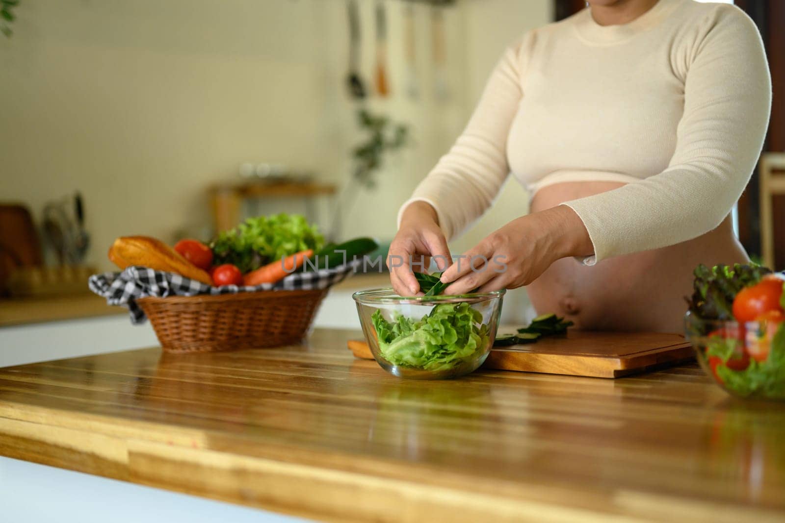 Pregnant woman preparing a fresh vegetable salad in the kitchen.