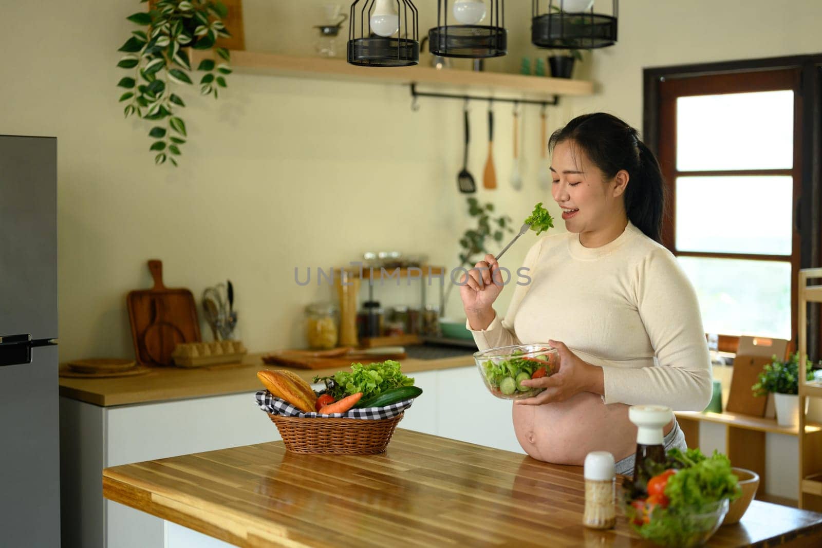 Smiling pregnant woman enjoying fresh vegetable salad in the kitchen. Healthy lifestyle concept.