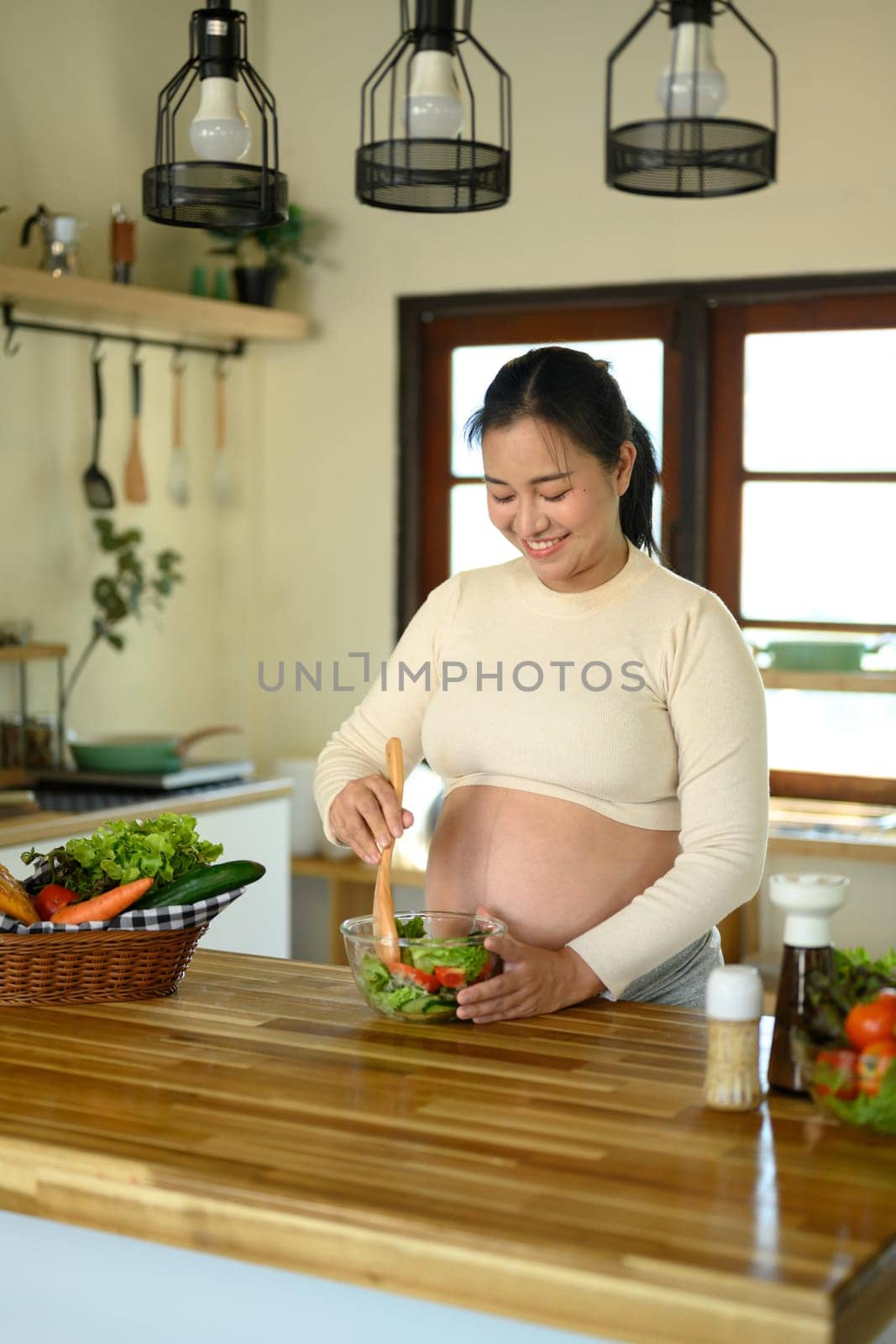 Pregnant woman preparing a fresh vegetable salad in the kitchen.