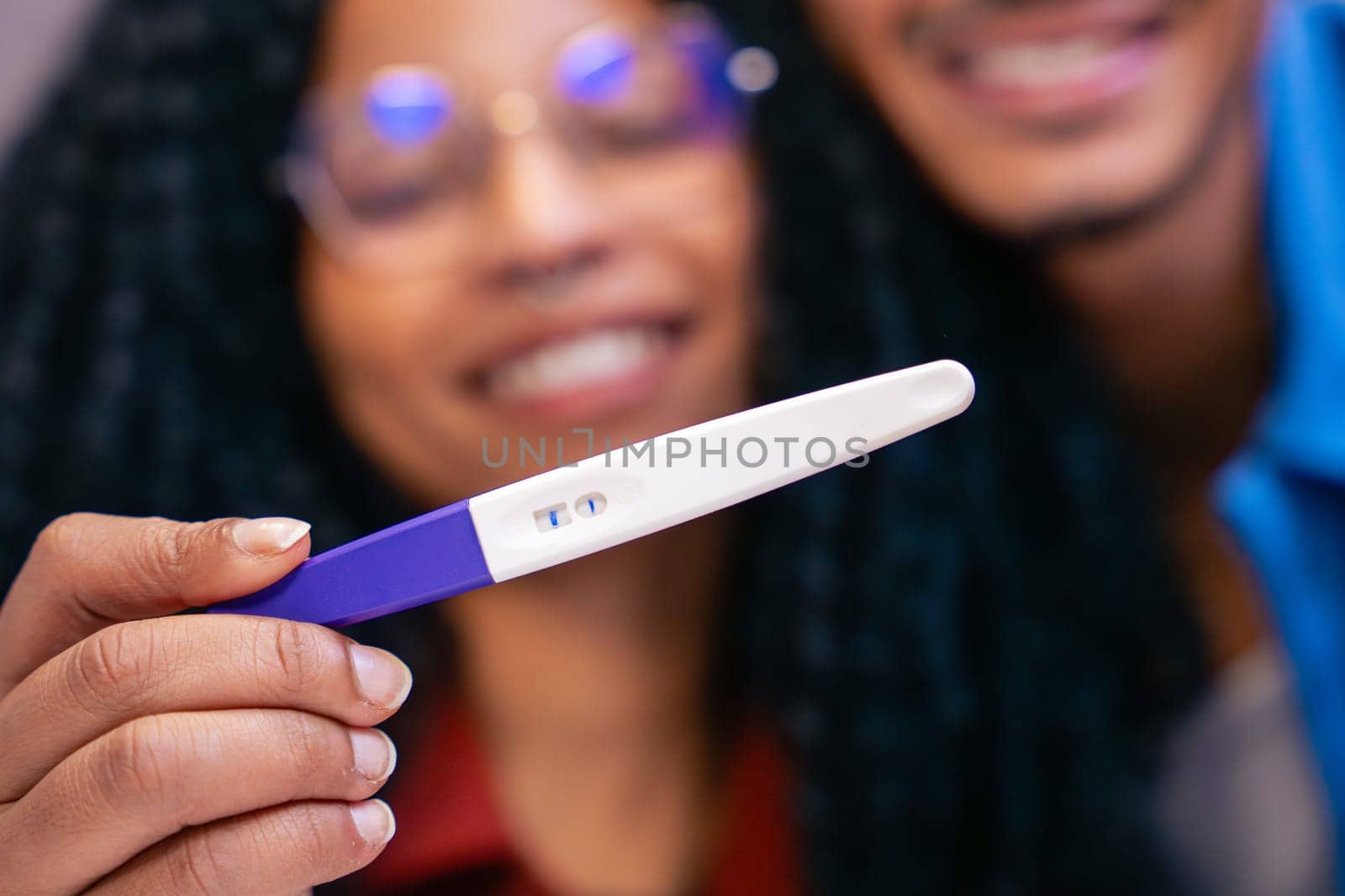 Close-up of a joyful couple smiling while holding a positive pregnancy test, celebrating the exciting news of expecting a baby. Concept of happiness, love, and new beginnings in family life.