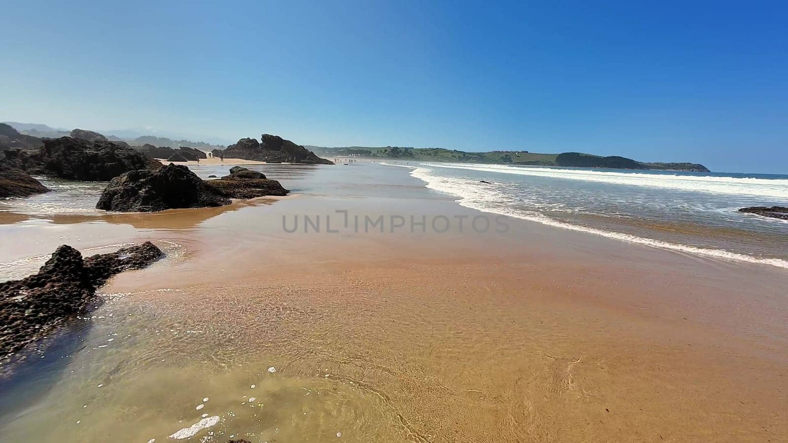 The stunning beach view showcases calm, gentle waves and unique rocky formations, all beneath a clear, blue sky