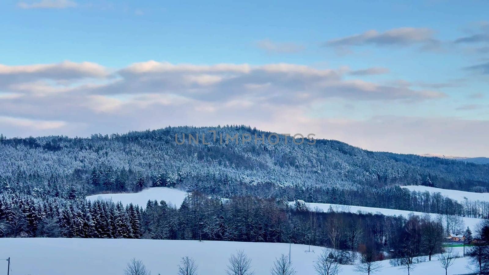 A beautifully peaceful and tranquil winter scene featuring hills blanketed with fresh snow under a clear blue sky