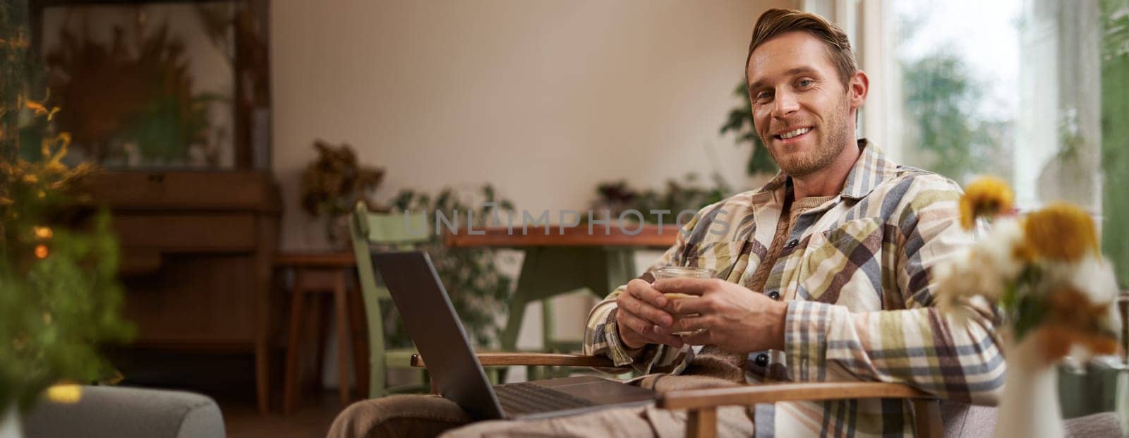 Handsome young professional, businessman sitting in cafe with glass of coffee and working on laptop, searching for inspiration outside of office workspace.