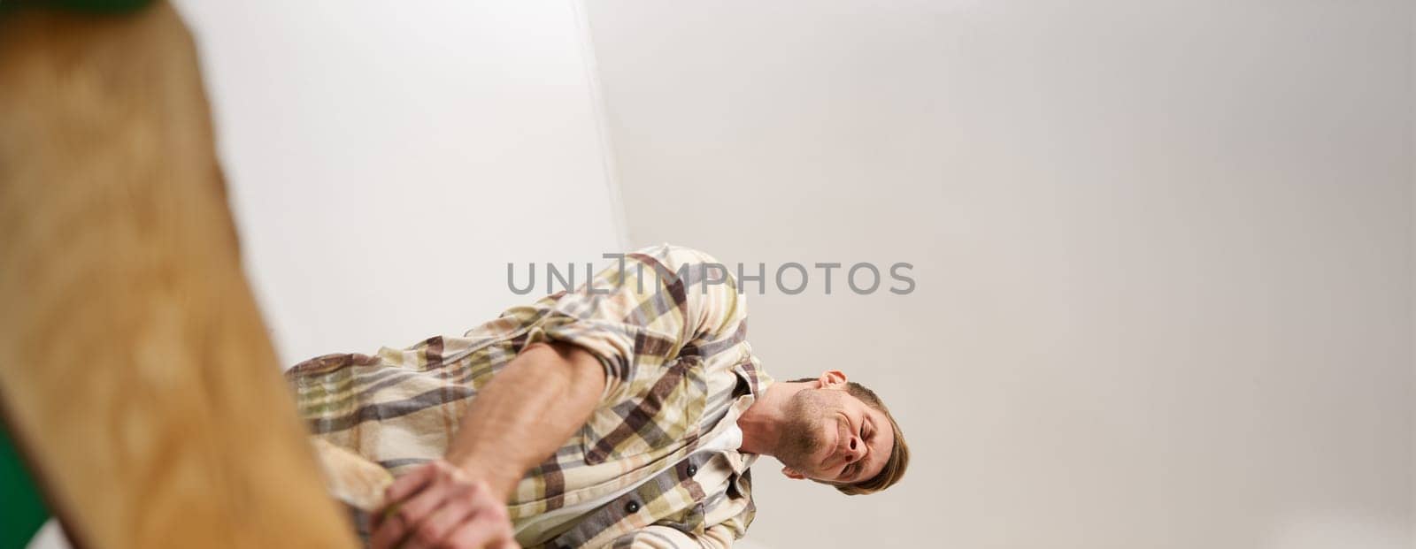 Image of funny man trying to close the suitcase filled with pile of clothes, packing luggage, putting things inside the bag. Tourism and traveller concept