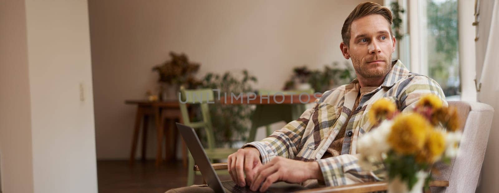 Portrait of handsome young man, working in cafe, sitting with laptop and coffee in hand, has remote job and using local co-working space instead of going to the office.