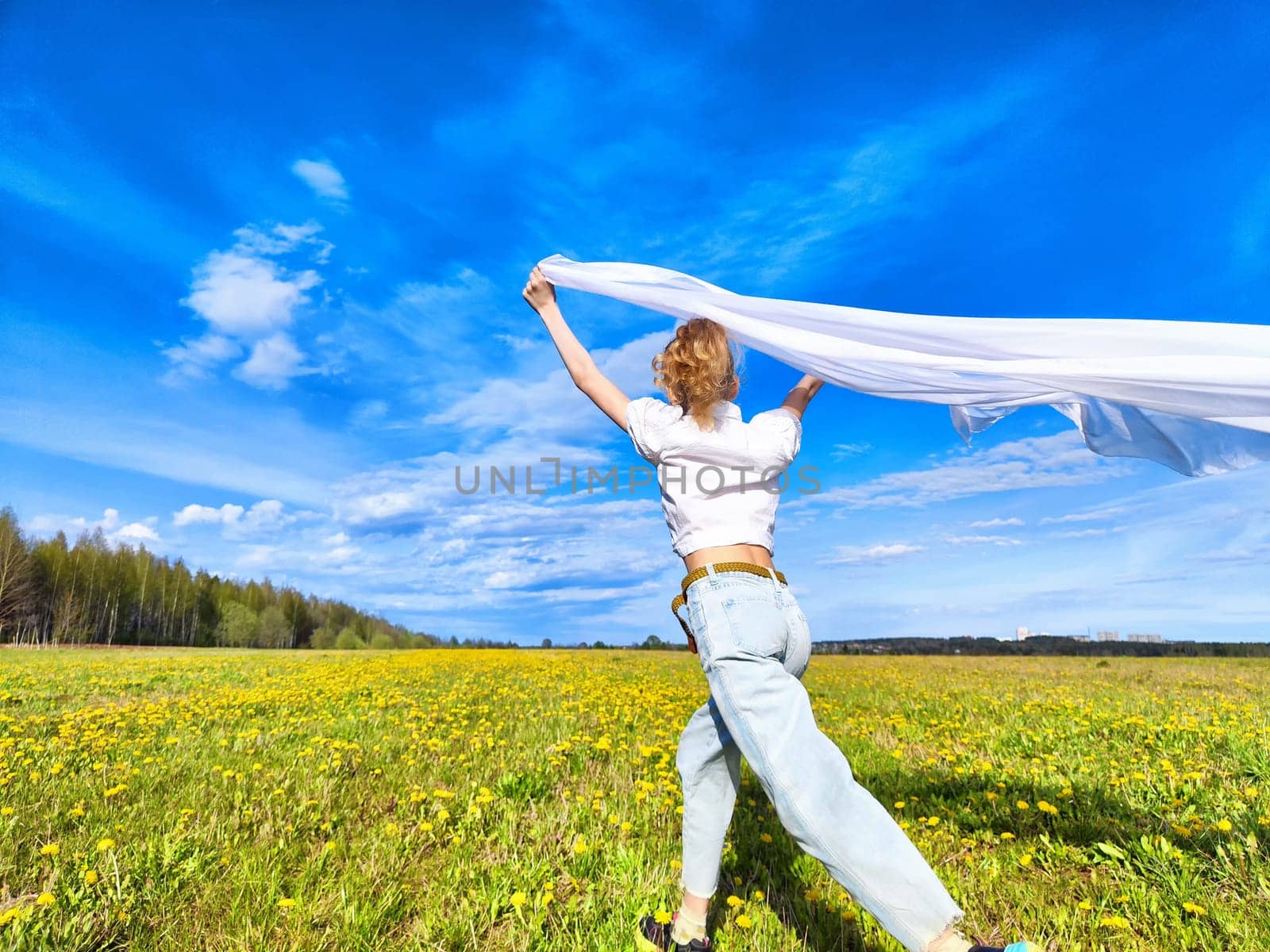 A joyful individual races across a blooming yellow flower field, waving a white scarf as they embrace the warmth of a beautiful day.