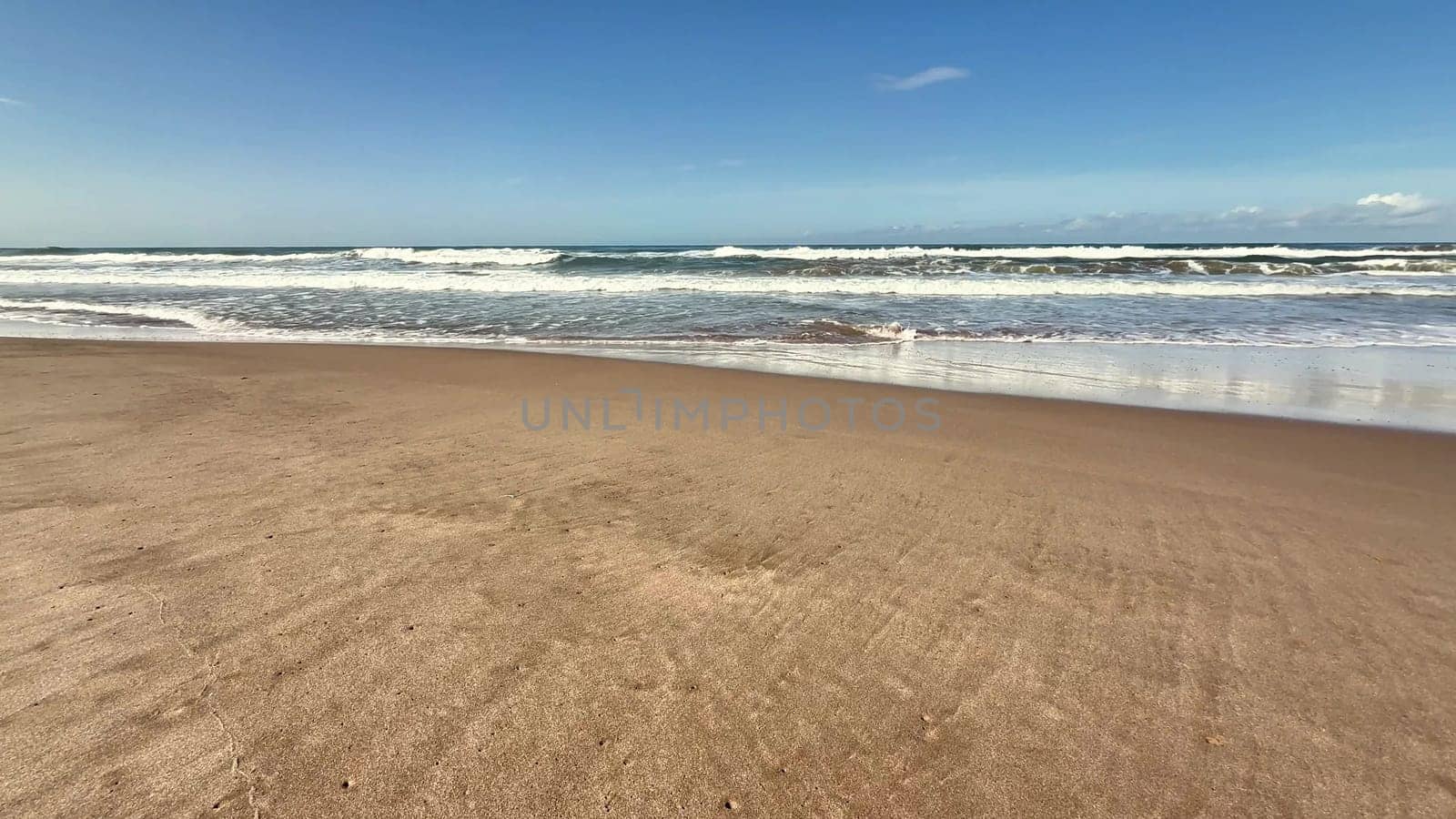 A serene beach scene with gentle waves lapping the shore beneath a bright blue sky and fluffy cotton clouds