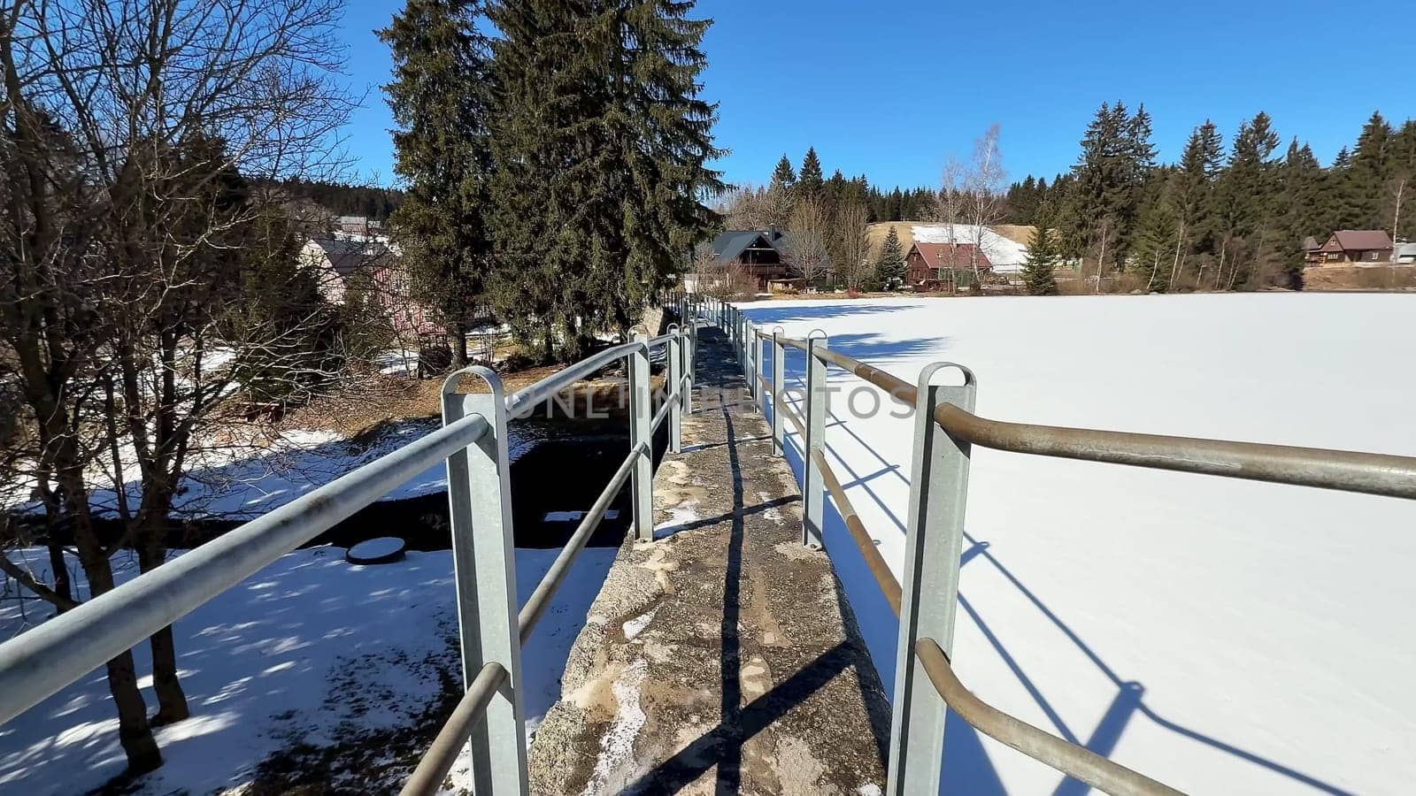 A stunningly beautiful snowy landscape showcases a winding pathway and tall trees beneath a bright clear blue sky