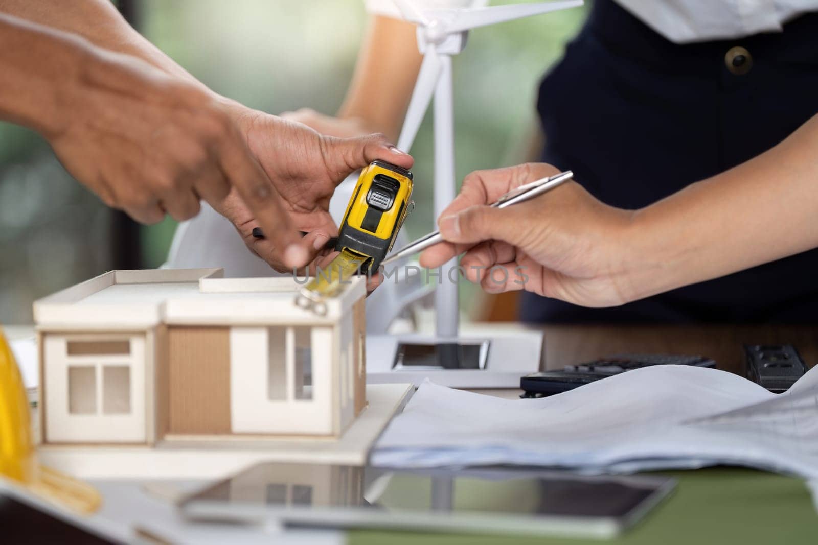 Engineers measuring a model house for sustainable construction, showcasing teamwork and innovative design planning.