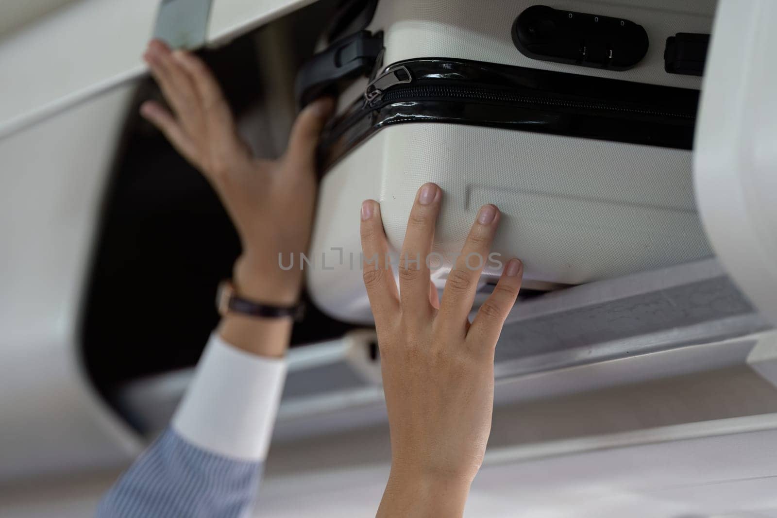 A focused traveler places her luggage in the overhead compartment while boarding the airplane, managing her belongings efficiently.
