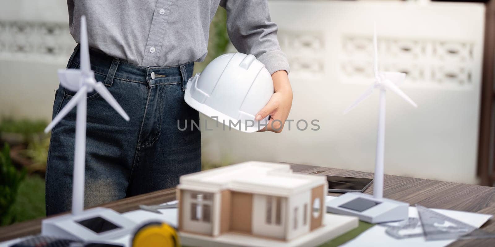 An engineer holding a helmet examines a sustainable architectural model featuring wind turbines, showcasing innovation in eco-friendly building design.