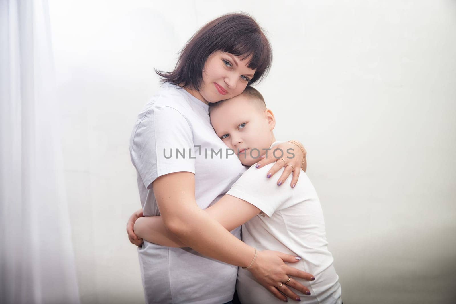 A mother and her son are hugging gently in a softly lit room, expressing affection and connection in a tender moment of love.