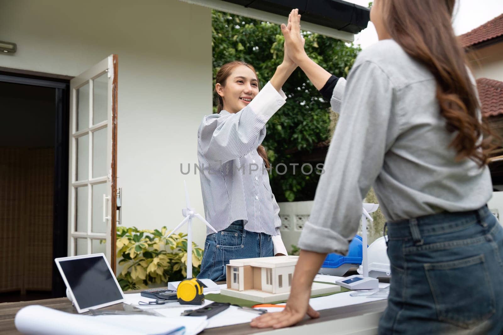 Two sustainability engineers share an encouraging high-five outdoors after discussing their innovative architectural project.