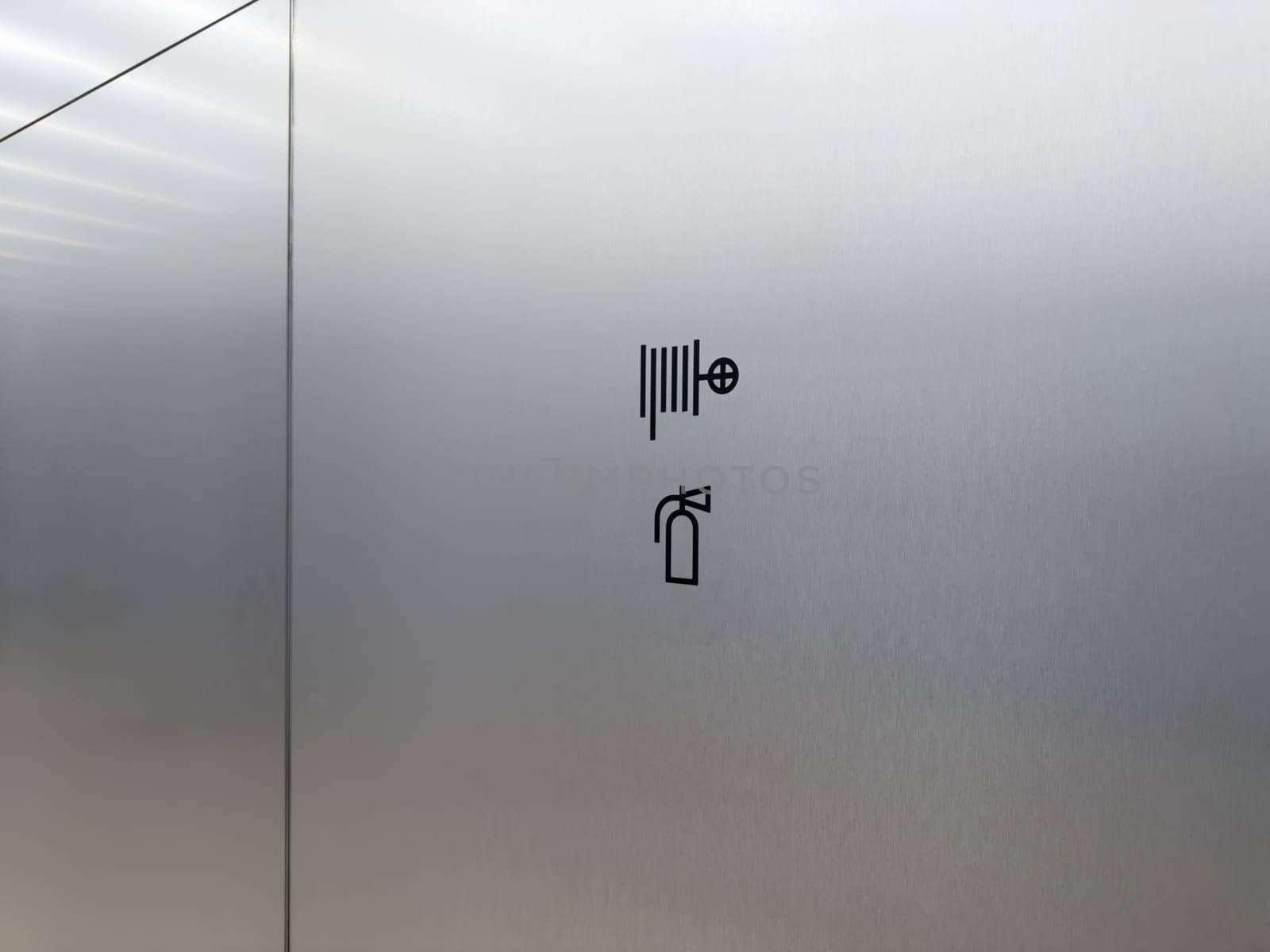 Minimal fire safety sign on metal wall. Black icon indicates location of fire hose and extinguisher. Emergency protection in public building or office interior
