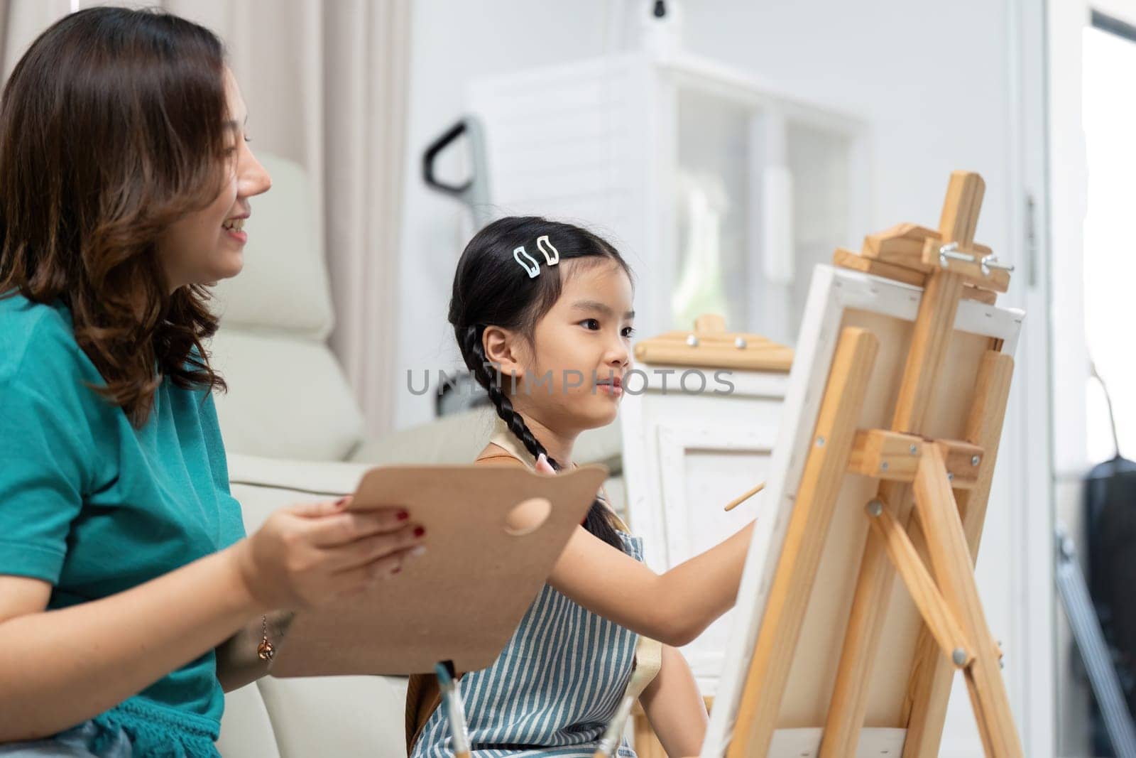 In a lively indoor setting, a mother and daughter paint together, sharing a creative and fun artistic experience.