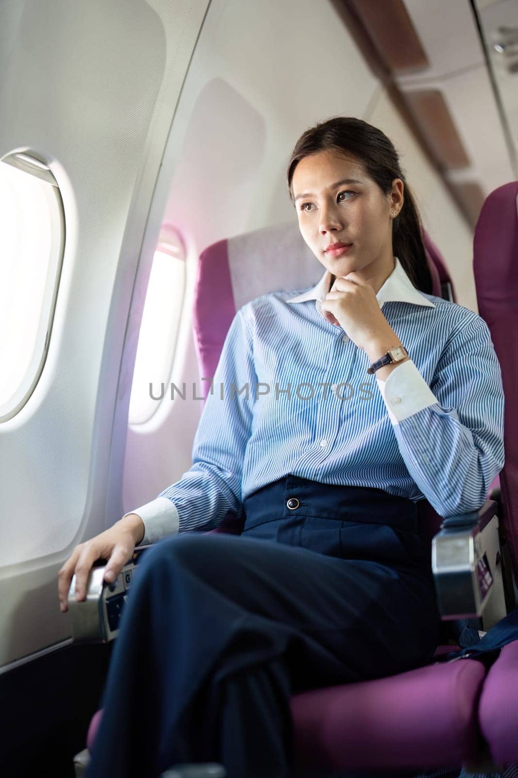 A thoughtful businesswoman seated in an airplane, gazing out the window and contemplating her journey ahead during business travel.