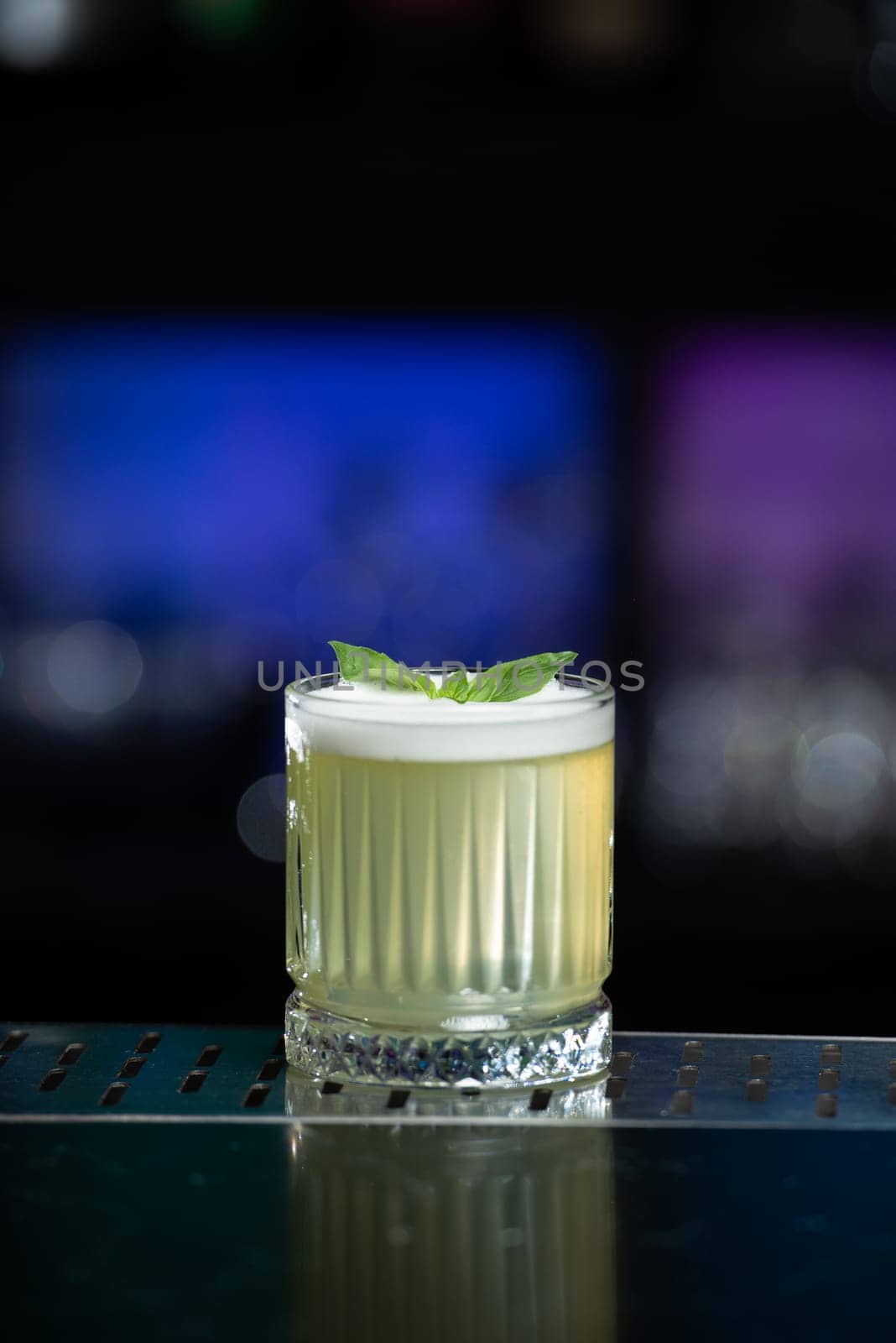The blurred background features hues of blue and purple with bokeh lights, a stylish bar