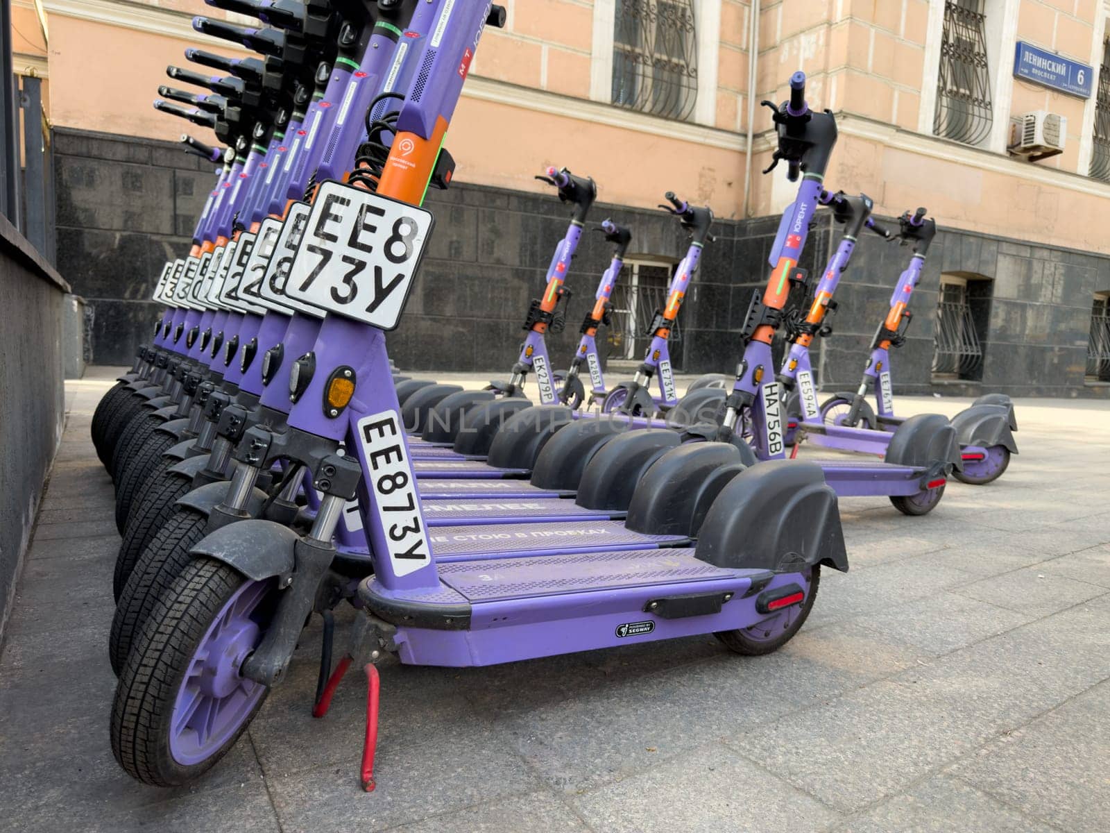 Moscow, Russia, April 24, 2025: Row of purple electric scooters parked in front of historical building on Leninsky Prospekt, showcasing rise of eco transport in modern city infrastructure