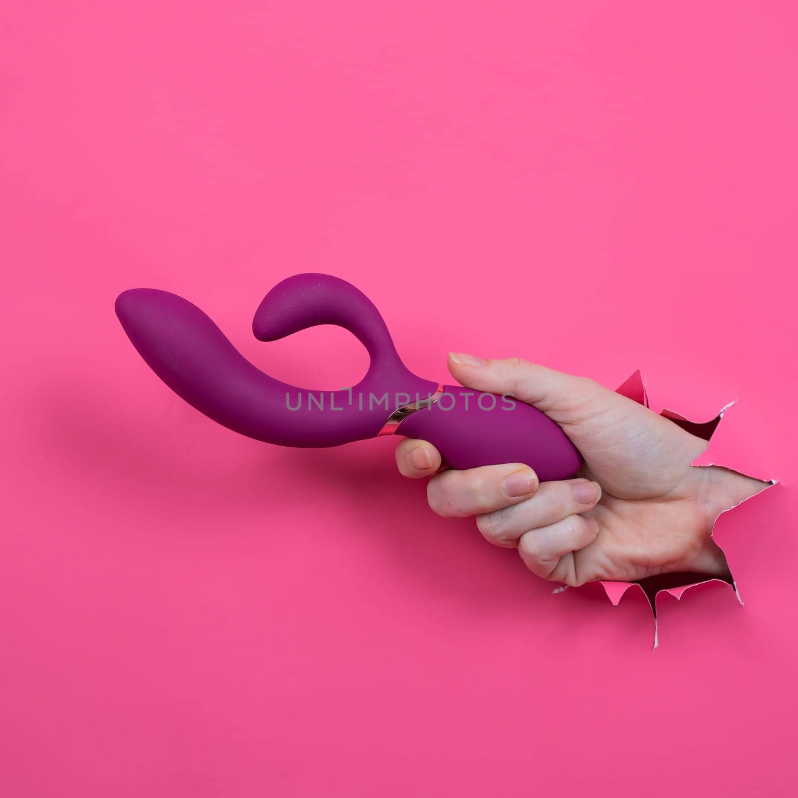 Female hand sticking out with raspberry sex toy from pink paper background