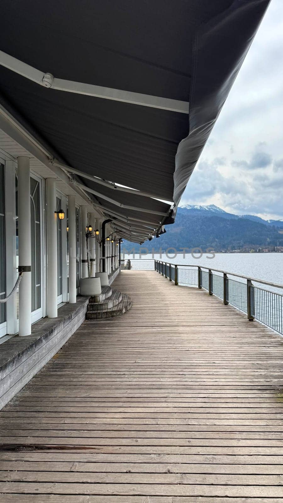 Wooden walkway stretches along the waterfront of Tegernsee lake in Germany, offering stunning views of mountains under a cloudy sky. The inviting atmosphere encourages relaxation and leisure activities for visitors and nature lovers, perfect for travel and nature enthusiasts, waterfront concept.