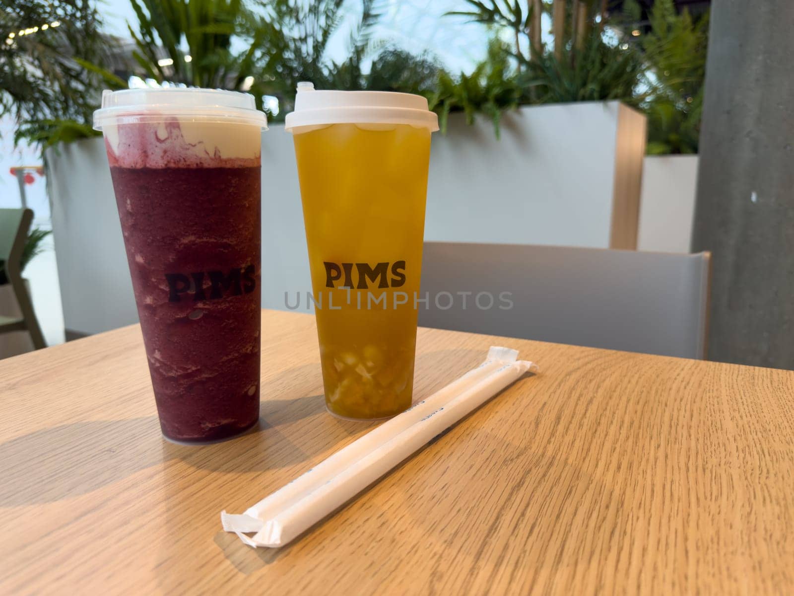 Moscow, Russia, April 25, 2025: Two takeaway drinks from PIMS cafe with paper straws on wooden table. Modern tea bar concept highlighting clean presentation and eco friendly details