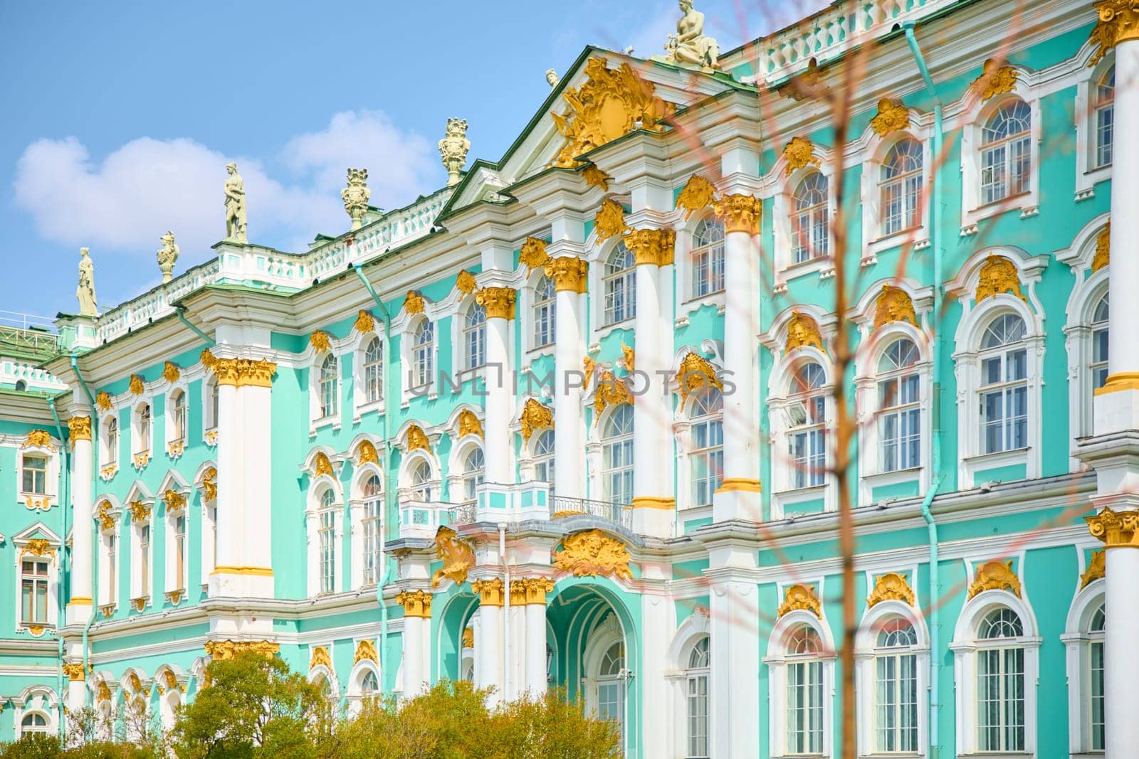 the incredibly picturesque facade of the Winter Palace through the branches of trees on a clear spring day, the heritage of Russia, the most famous landmark of St. Petersburg, the museum. High quality photo