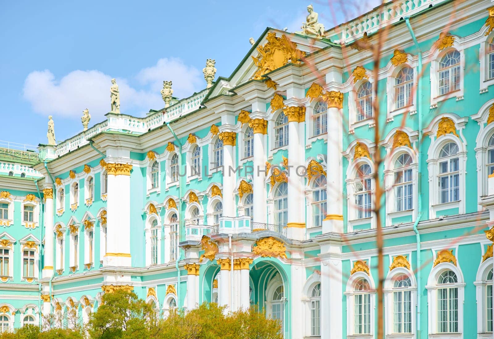 the incredibly picturesque facade of the Winter Palace through the branches of trees on a clear spring day, the heritage of Russia, the most famous landmark of St. Petersburg, the museum. High quality photo