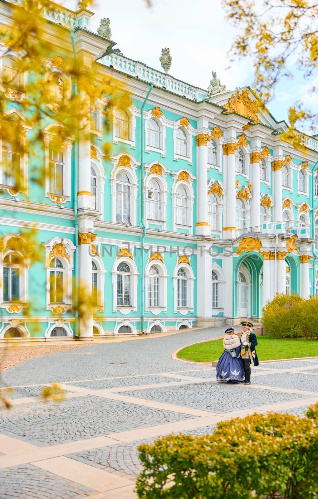 Russia, St. Petersburg, 10 May 2025: the incredibly picturesque facade of the Winter Palace through the branches of trees on a clear spring day, actors in tsarist outfits, the heritage of Russia. High quality photo
