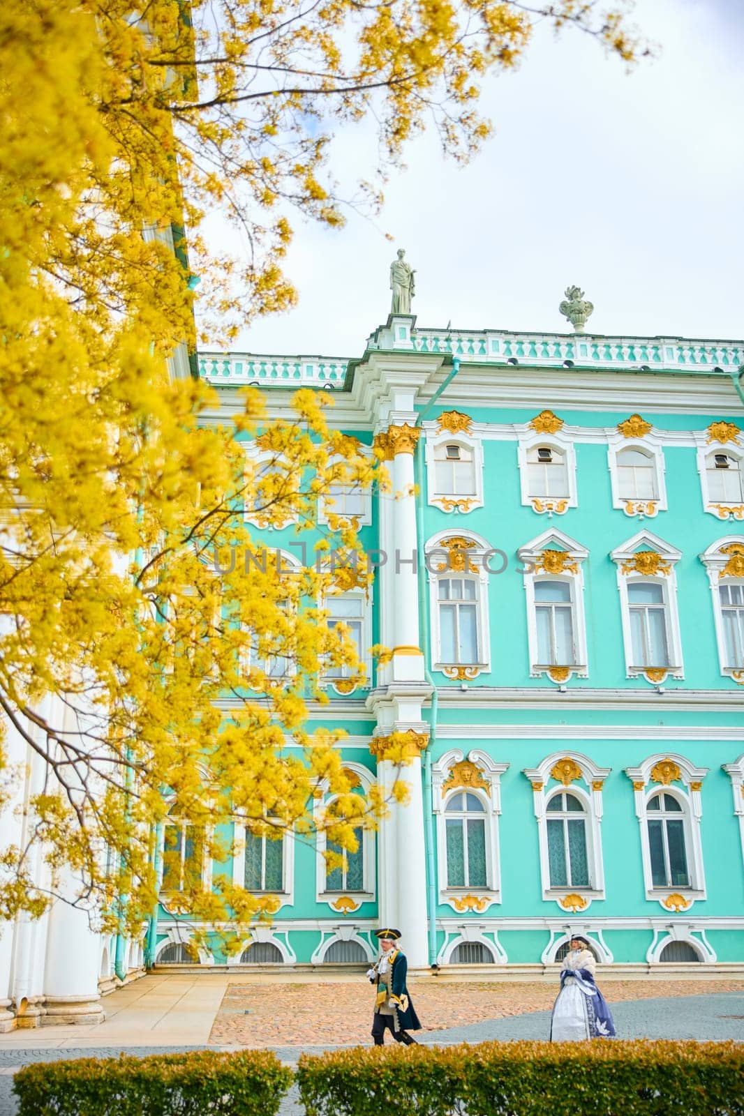 Russia, St. Petersburg, 10 May 2025: the incredibly picturesque facade of the Winter Palace through the branches of trees on a clear spring day, actors in tsarist outfits, the heritage of Russia. High quality photo