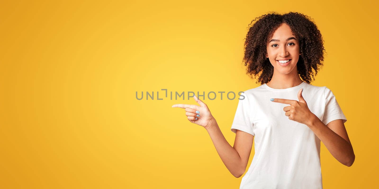 People sincere emotions, lifestyle and best choice concept. Cheerful african american lady in white t-shirt points fingers towards empty space isolated on orange background, studio shot