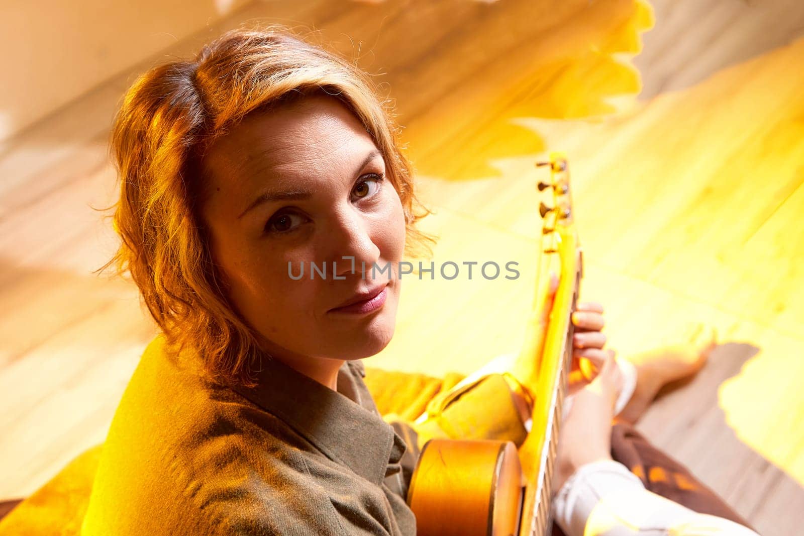 A woman sits comfortably with a guitar, surrounded by soft warm light while expressing her musical talent in an inviting space.