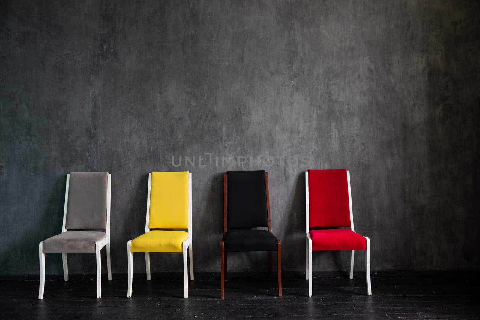 Four old chairs of different colors in the interior of a gray room