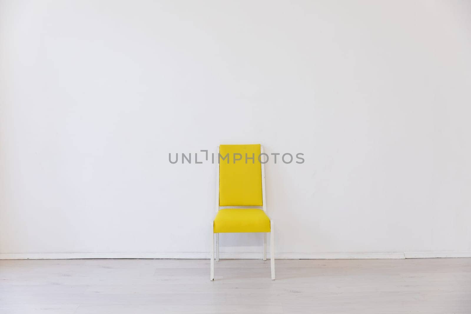 One yellow old chair in the interior of a white room near the wall