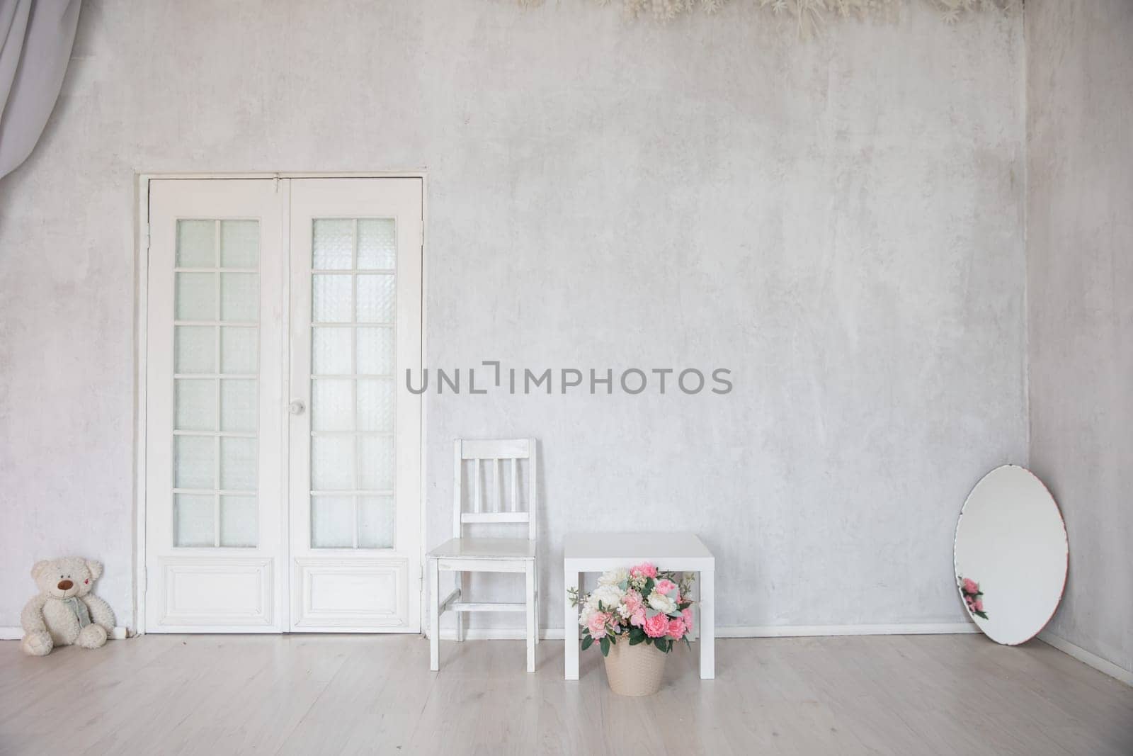 Table with a vase of flowers and a bear toy in the interior of a room with a door
