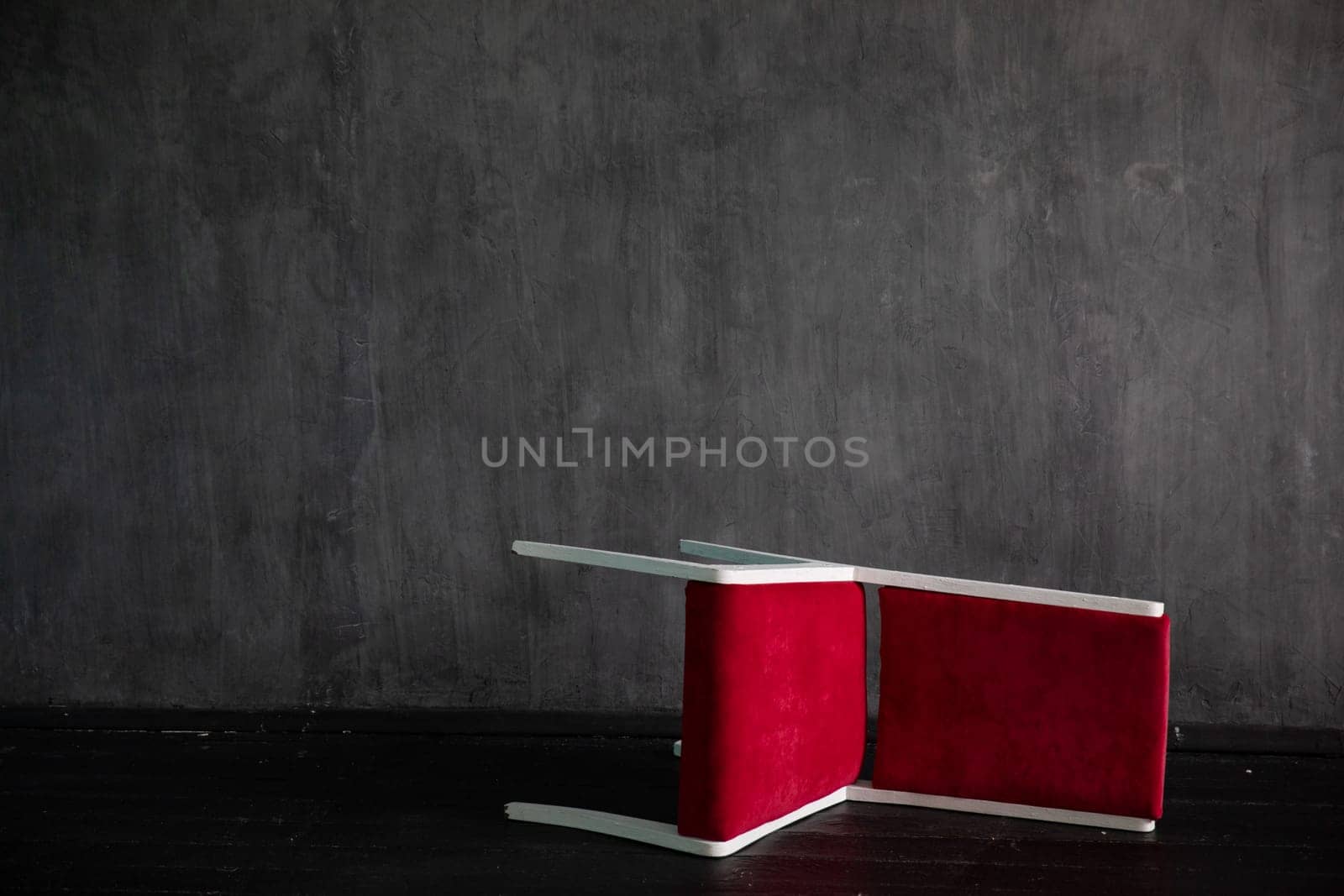 A red chair fell on the black floor of a gray room