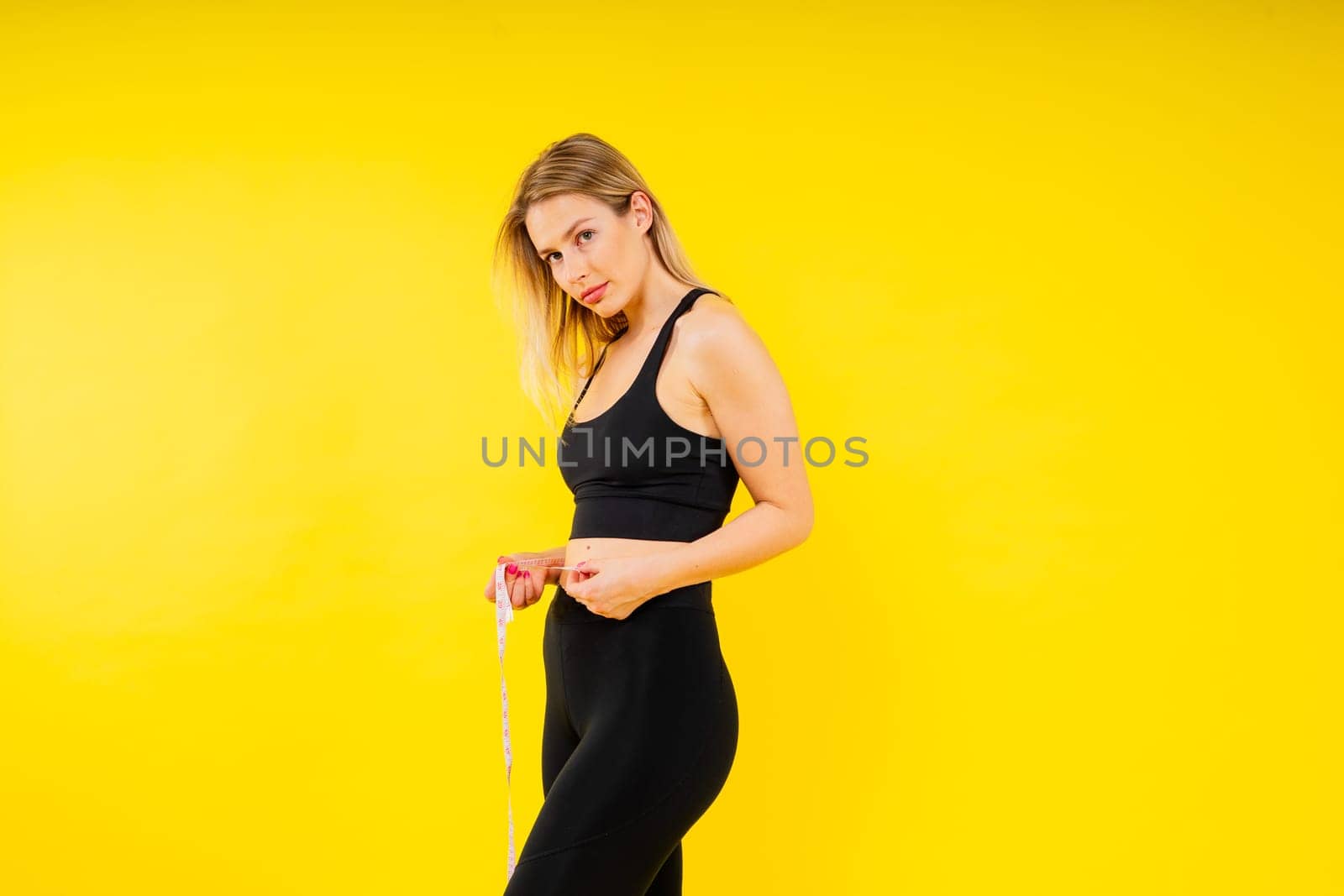 Slim body of fitness woman in a sportswear with measuring tape on waist against studio background
